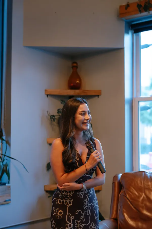 Smiling woman in patterned dress speaking into microphone at an indoor event in Charlotte, NC.