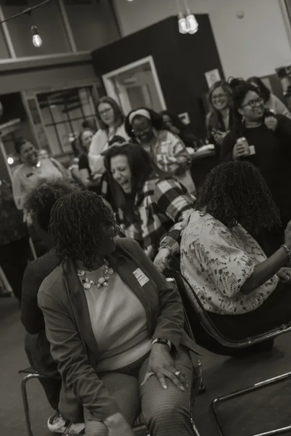 Black and white photo of diverse women laughing and networking at a lively event in Charlotte.