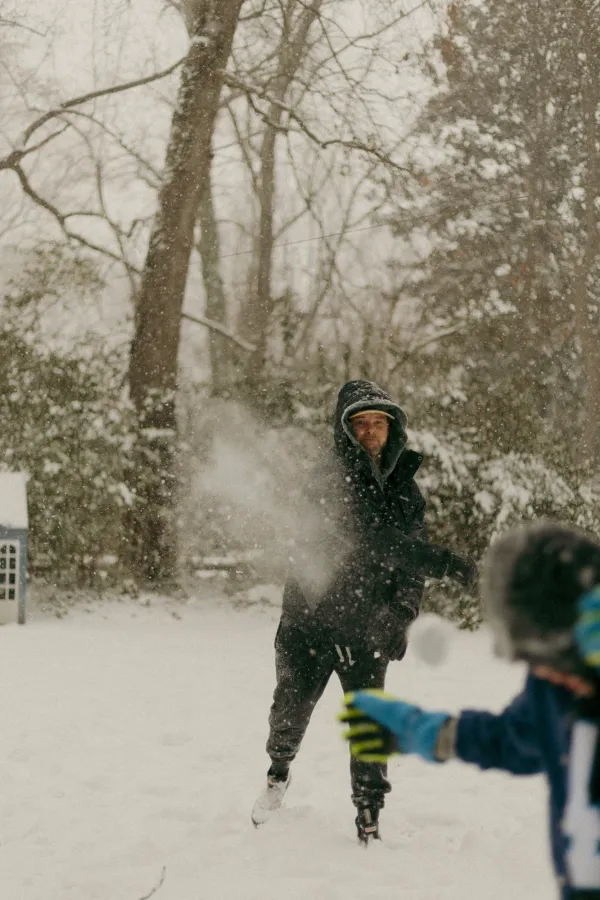 Man laughing during a snowball fight in a snowy Charlotte backyard, snow falling around him.
