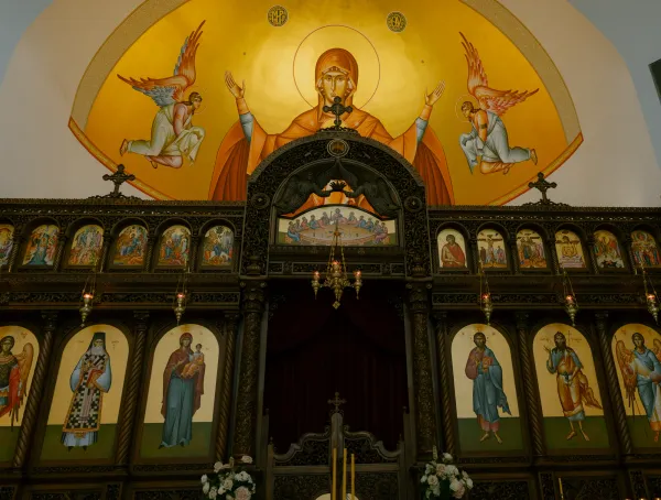 Detailed Orthodox church iconostasis with icons and a large mural of the Virgin Mary and angels.