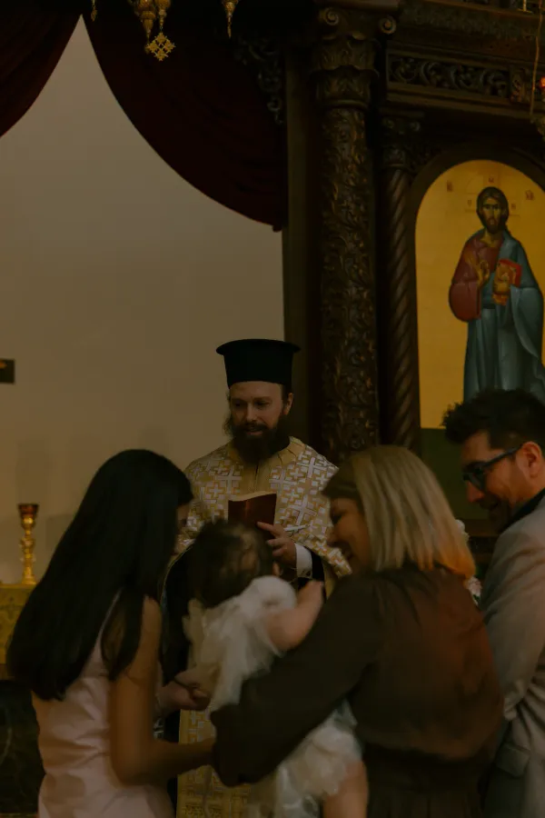 Priest performing a christening ceremony with a baby and family in a Charlotte church.