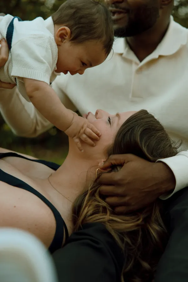 Baby reaches for mother's face while father holds baby, tender family moment.