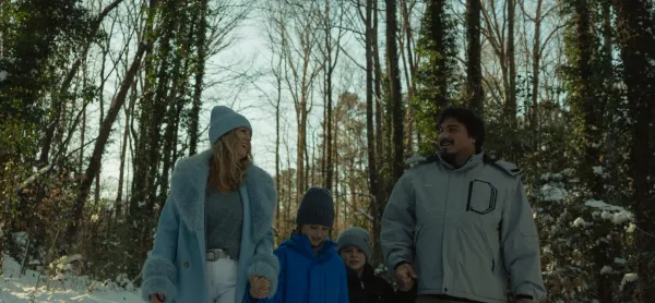 Happy family, parents holding hands with two children, walking in a snowy forest in winter.