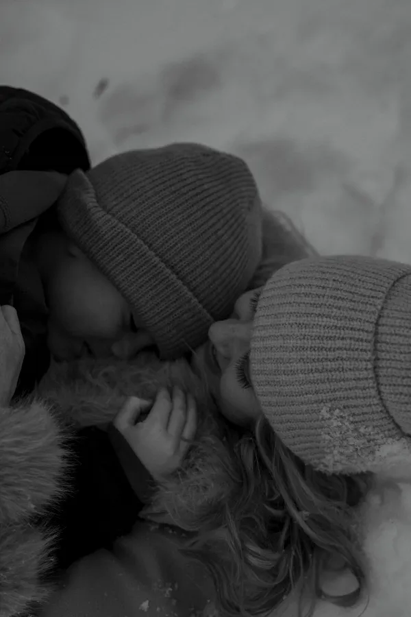 Black and white close-up of a couple in beanies, snuggled together in snow.