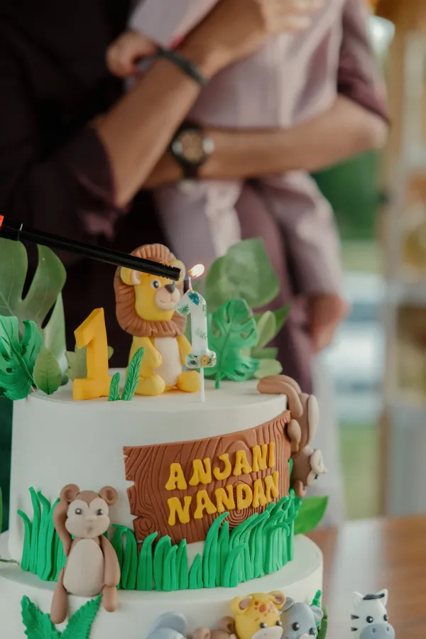 Close-up of a jungle safari themed first birthday cake with a lit '1' candle and fondant animals.