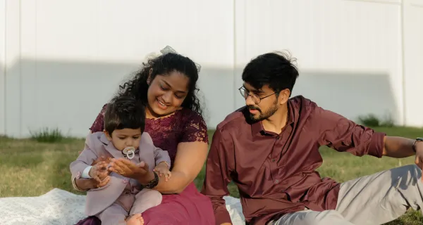Happy family with baby in suit sitting on grass outdoors, smiling and interacting.