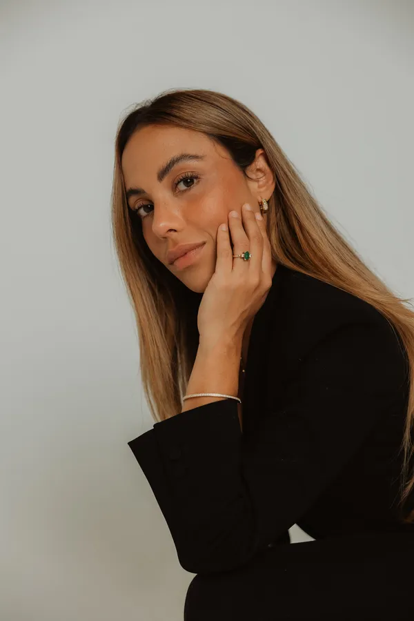 Close-up professional branding portrait of a confident woman with long brown hair, wearing a black blazer and elegant jewelry, looking directly at the camera.