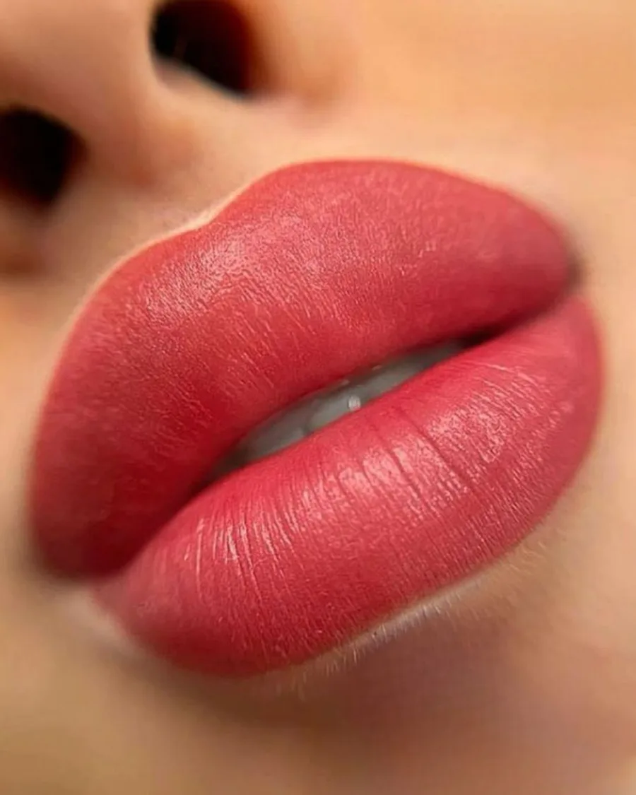 Nahaufnahme von perfekt pigmentierten Lippen in einem kräftigen Korallrot, Ergebnis einer PMU-Schulung für Lippenpigmentierun