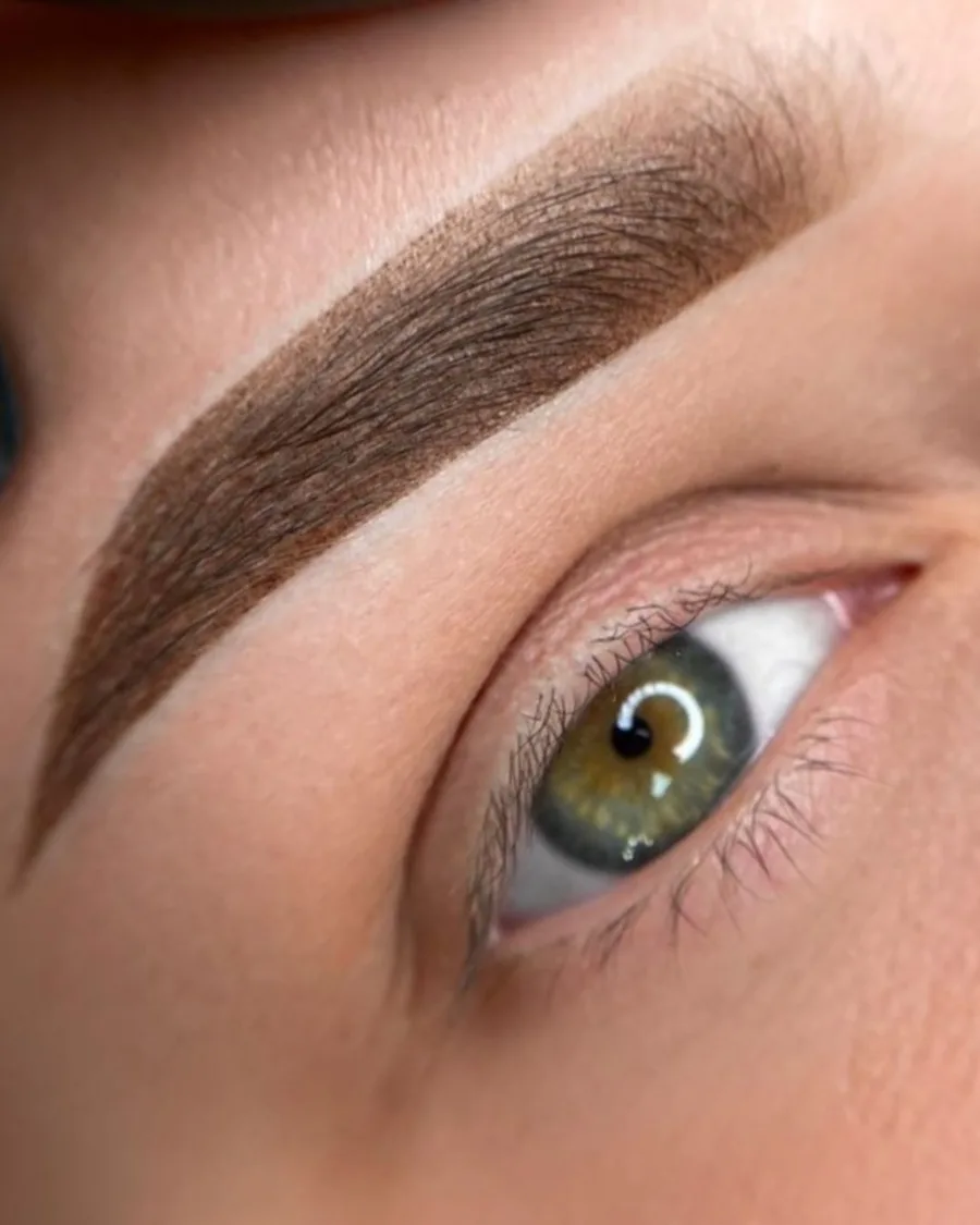 Nahaufnahme einer perfekt gestylten Augenbraue mit Powder Brows Effekt und grünem Auge nach einer PMU-Schulung
