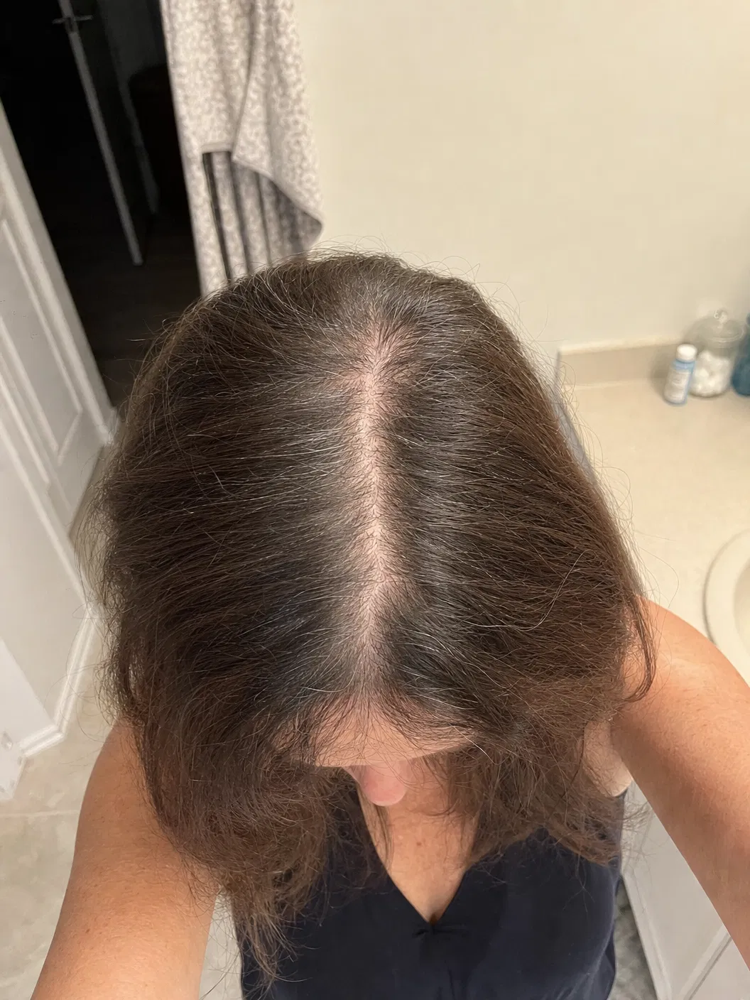 UGC style photo of a woman over 30 showing a wider-looking hair part in bathroom lighting