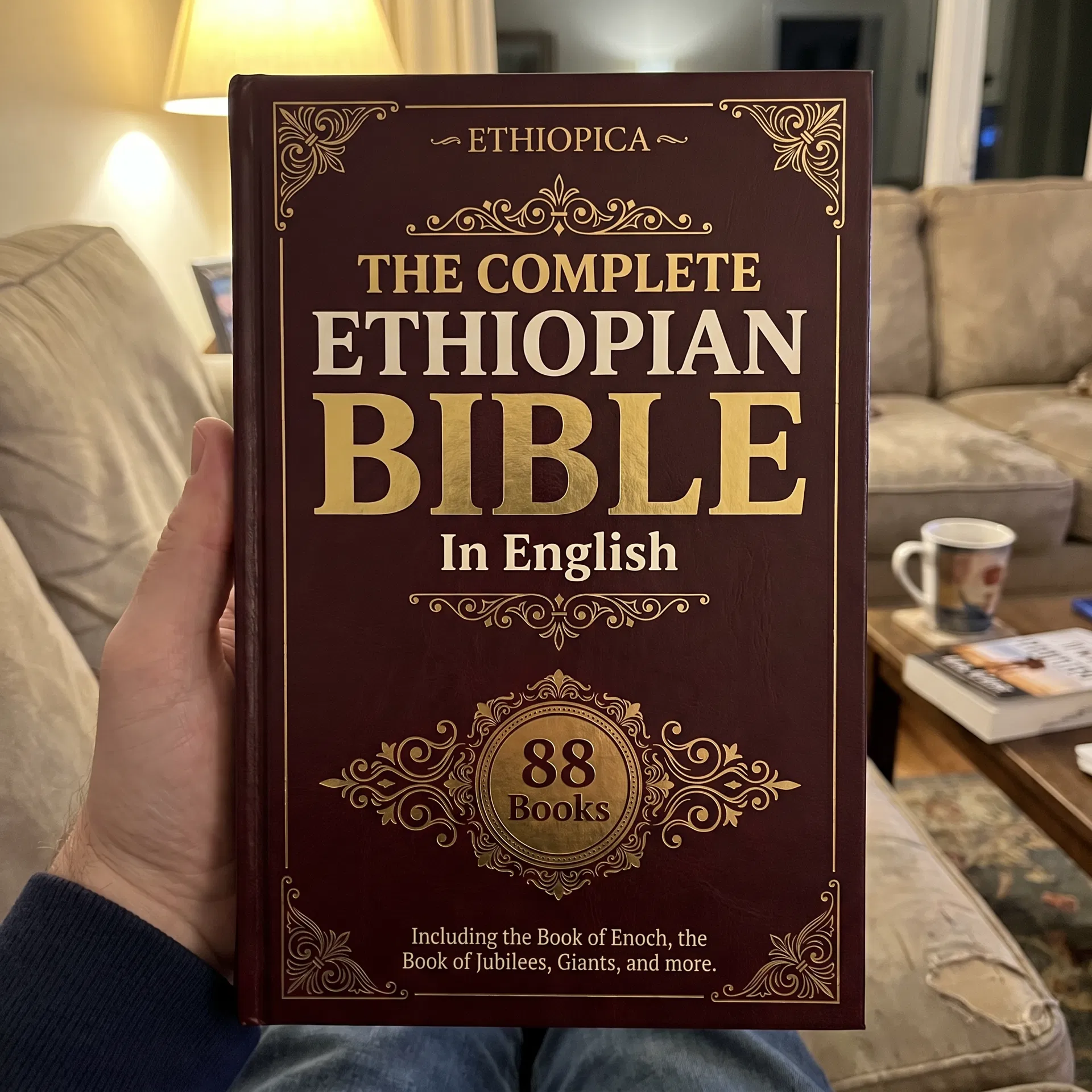 A man holding the closed Complete Ethiopian Bible up to the camera, gold foil cover catching the light