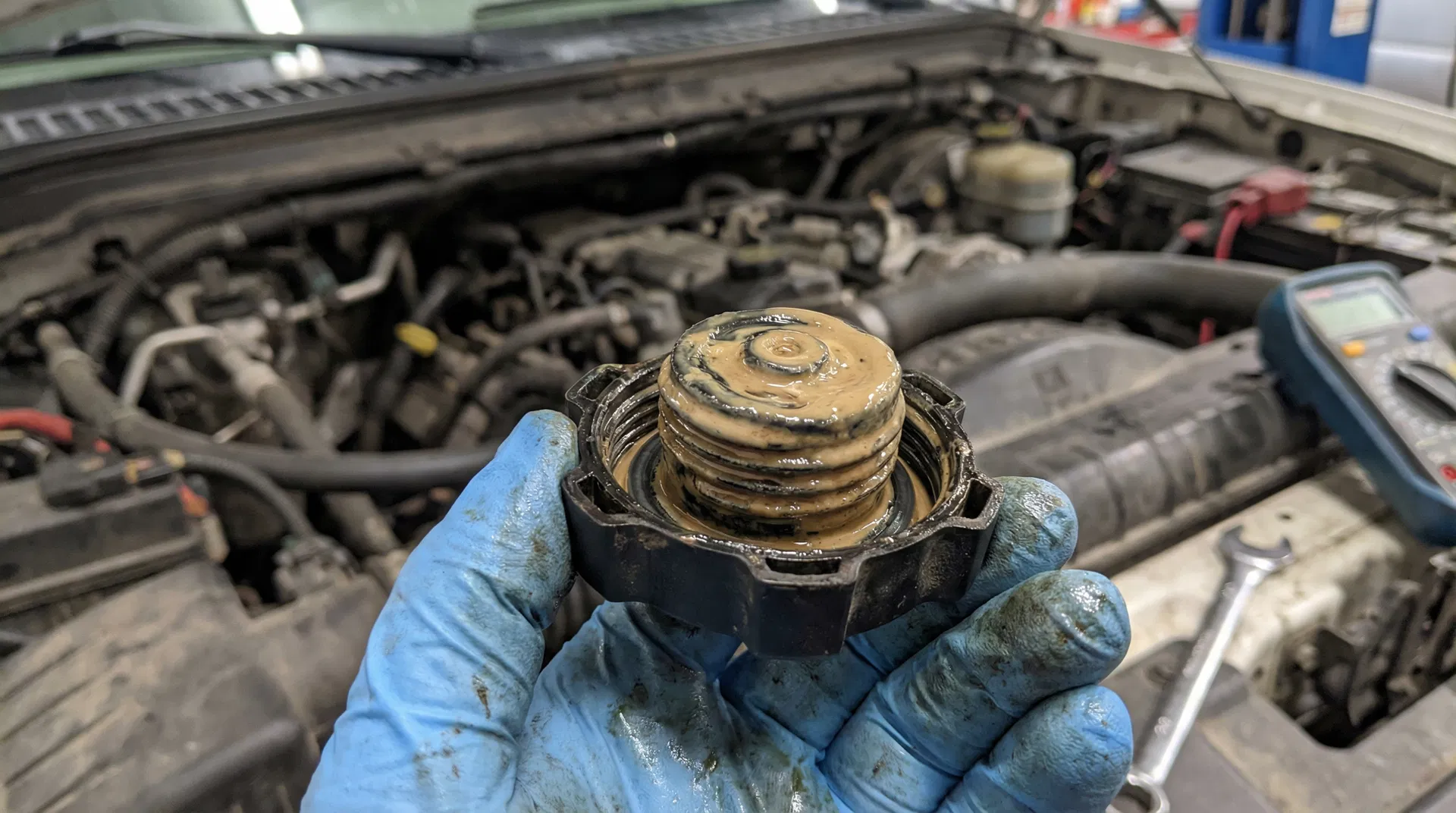 Coolant reservoir cap showing milky brownish sludge — a classic sign of oil cooler failure
