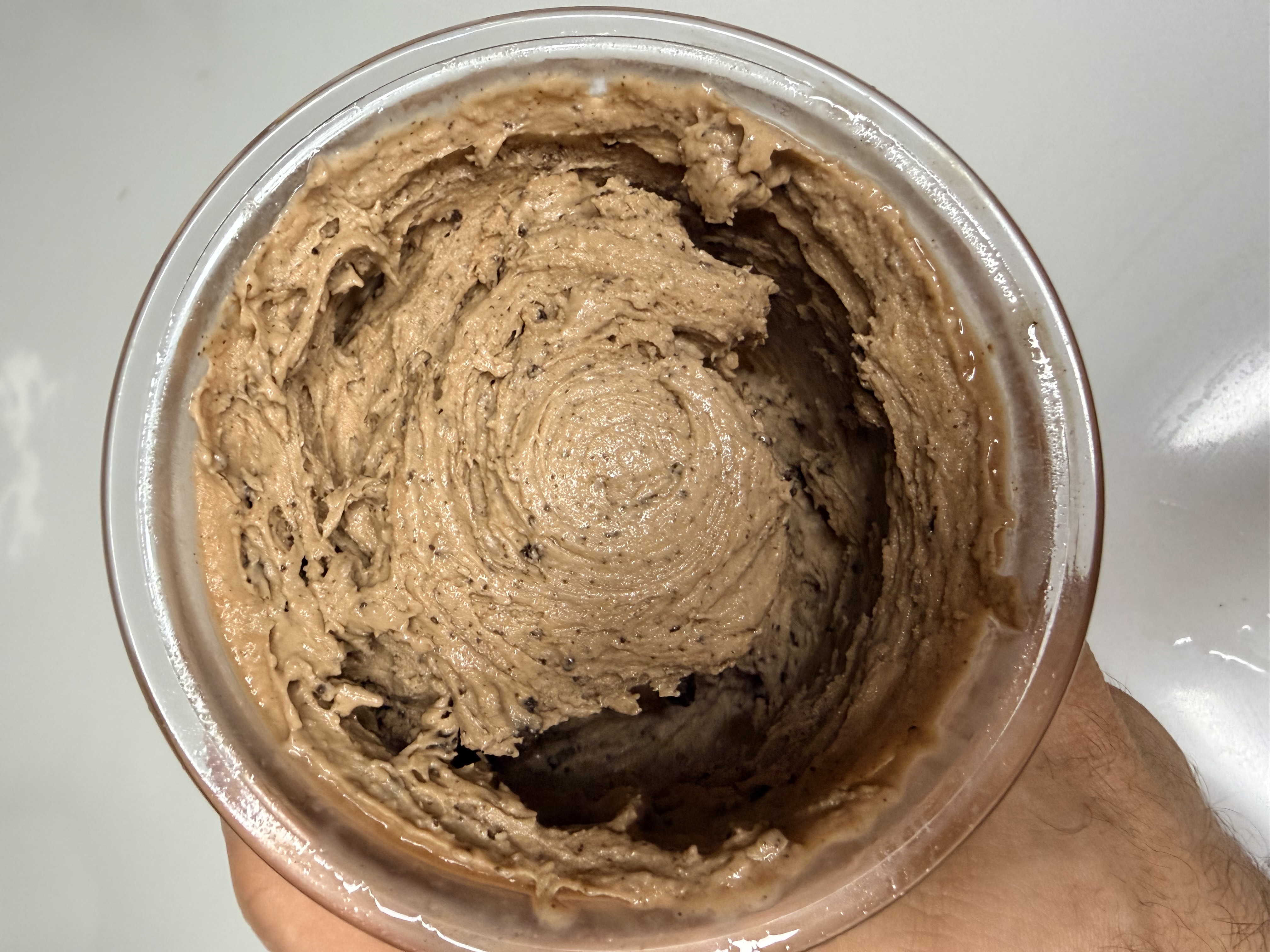 Scooping creamy Ninja Creami cookies and cream protein ice cream from a clear pint with a hand. 2