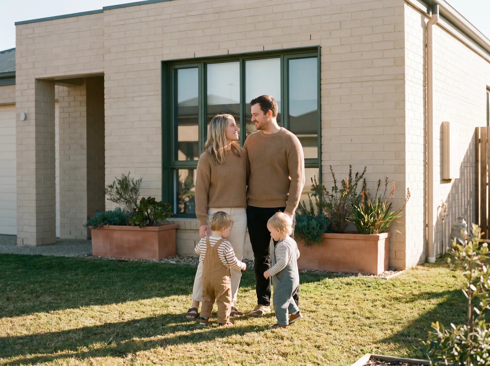 Family on the lawn of a modern brick home in golden hour light