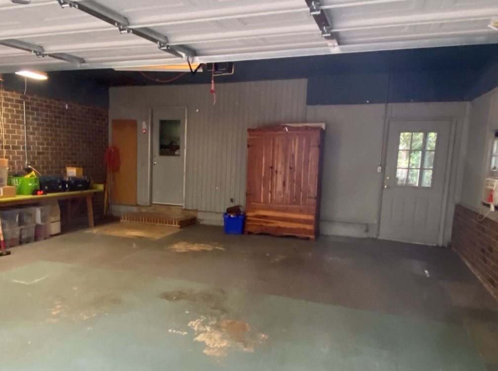 A functional garage interior with a workbench, storage cabinet, and two doors, featuring a concrete floor and mixed brick and painted walls.