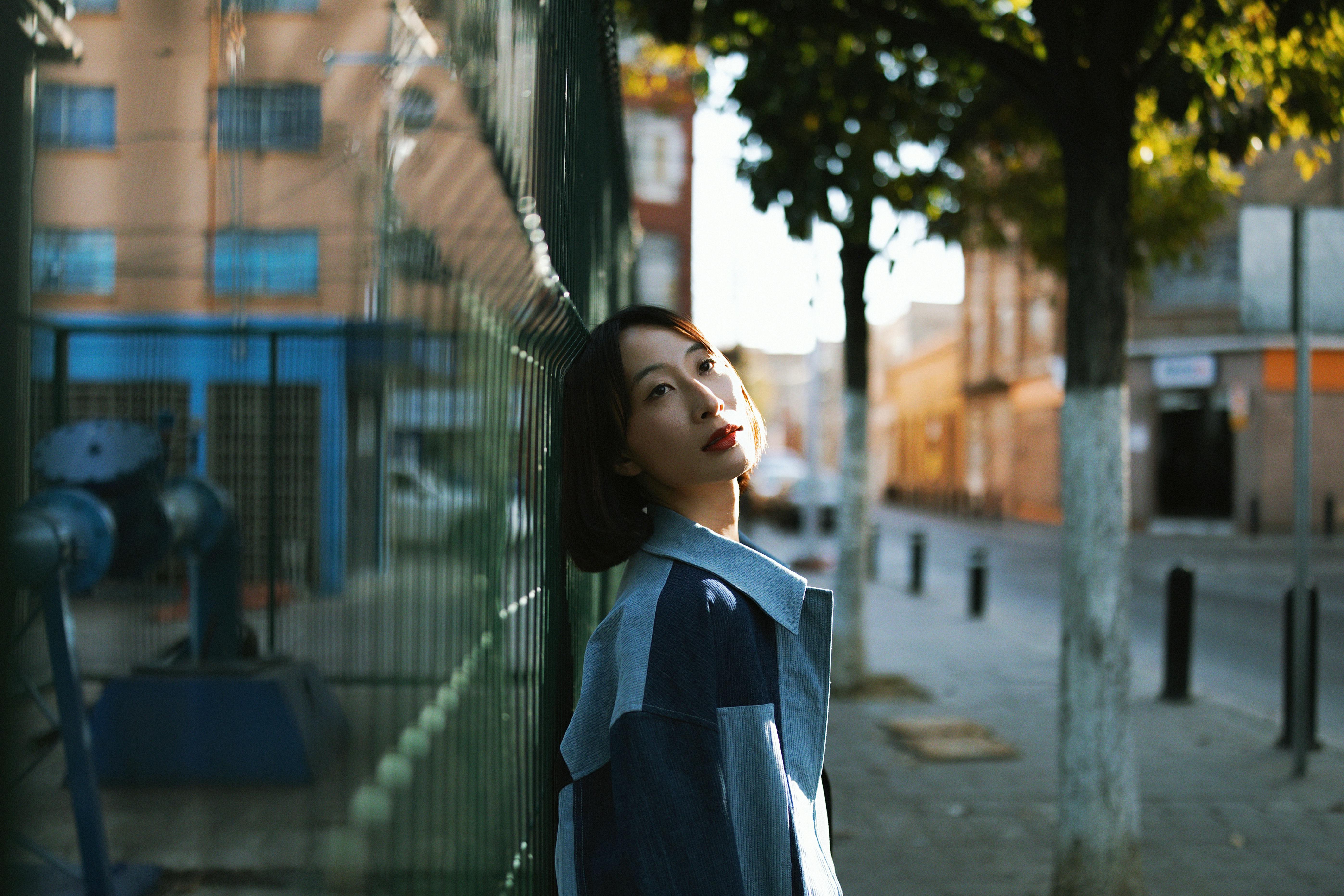 Woman in blue jacket by green fence
