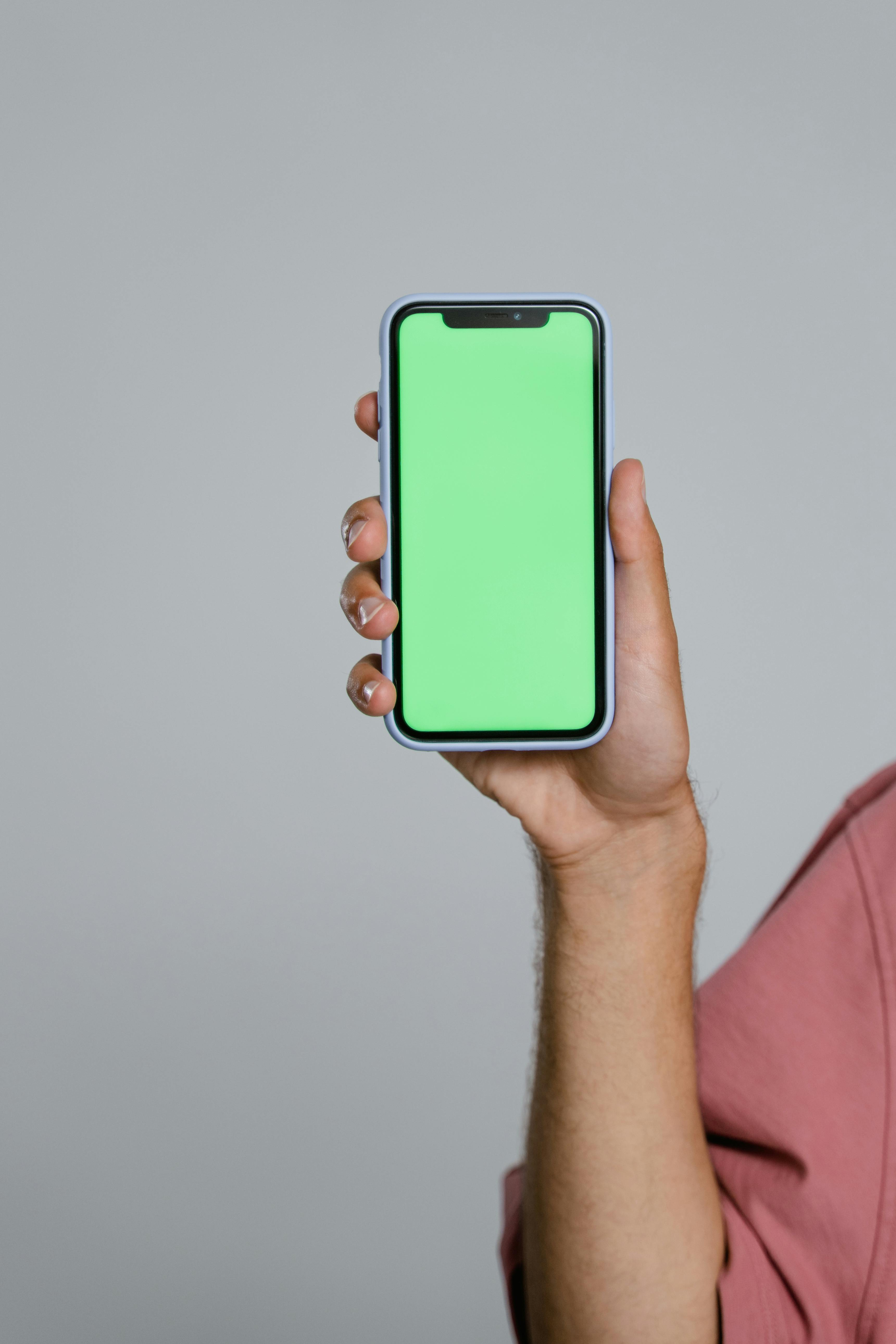 Hand holding smartphone with green screen display