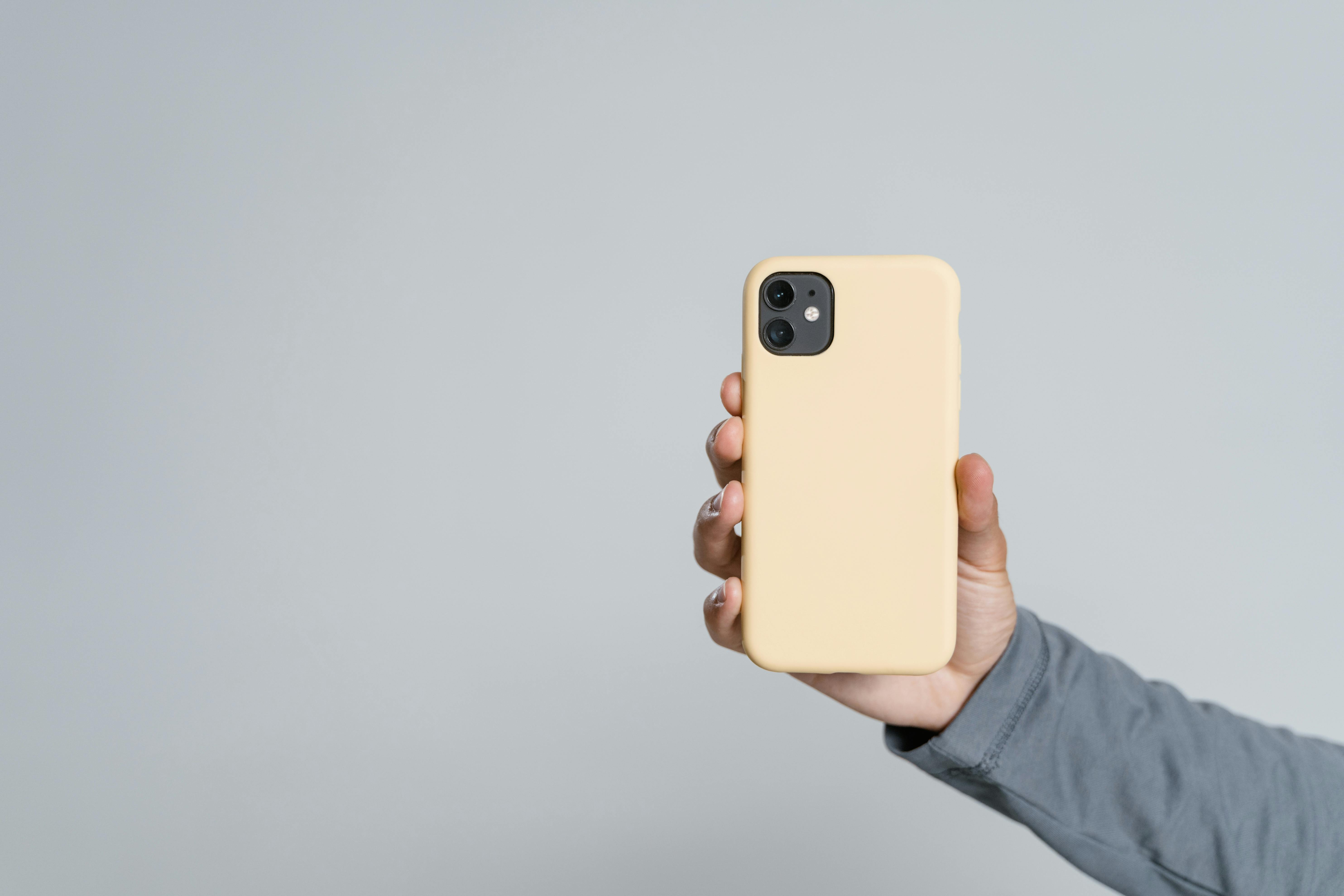 Hand holding smartphone with yellow case against grey background