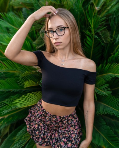 Young Woman in Glasses Posing Against Lush Greenery