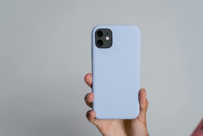 Hand holding light blue smartphone against grey background