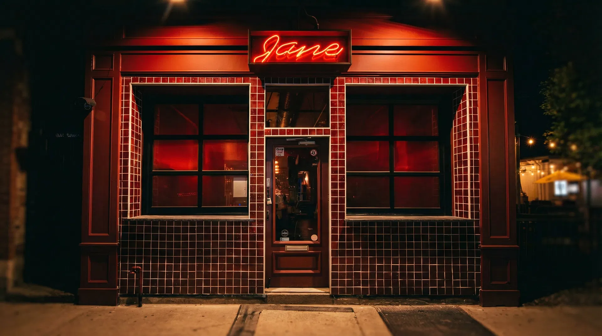 Jane cocktail bar storefront at night with red neon sign, dark red tile facade, and warm interior glow in Louisville's NuLu district