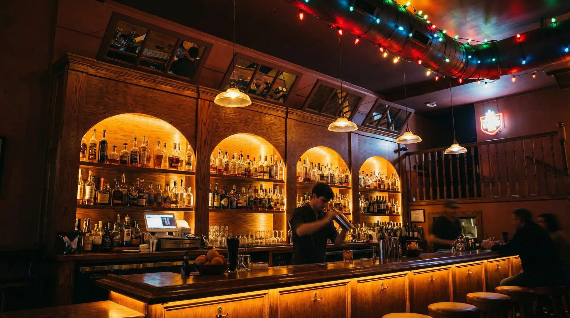 Jane's warm interior with arched wooden shelves filled with spirits, colorful string lights, and bartender mixing cocktails