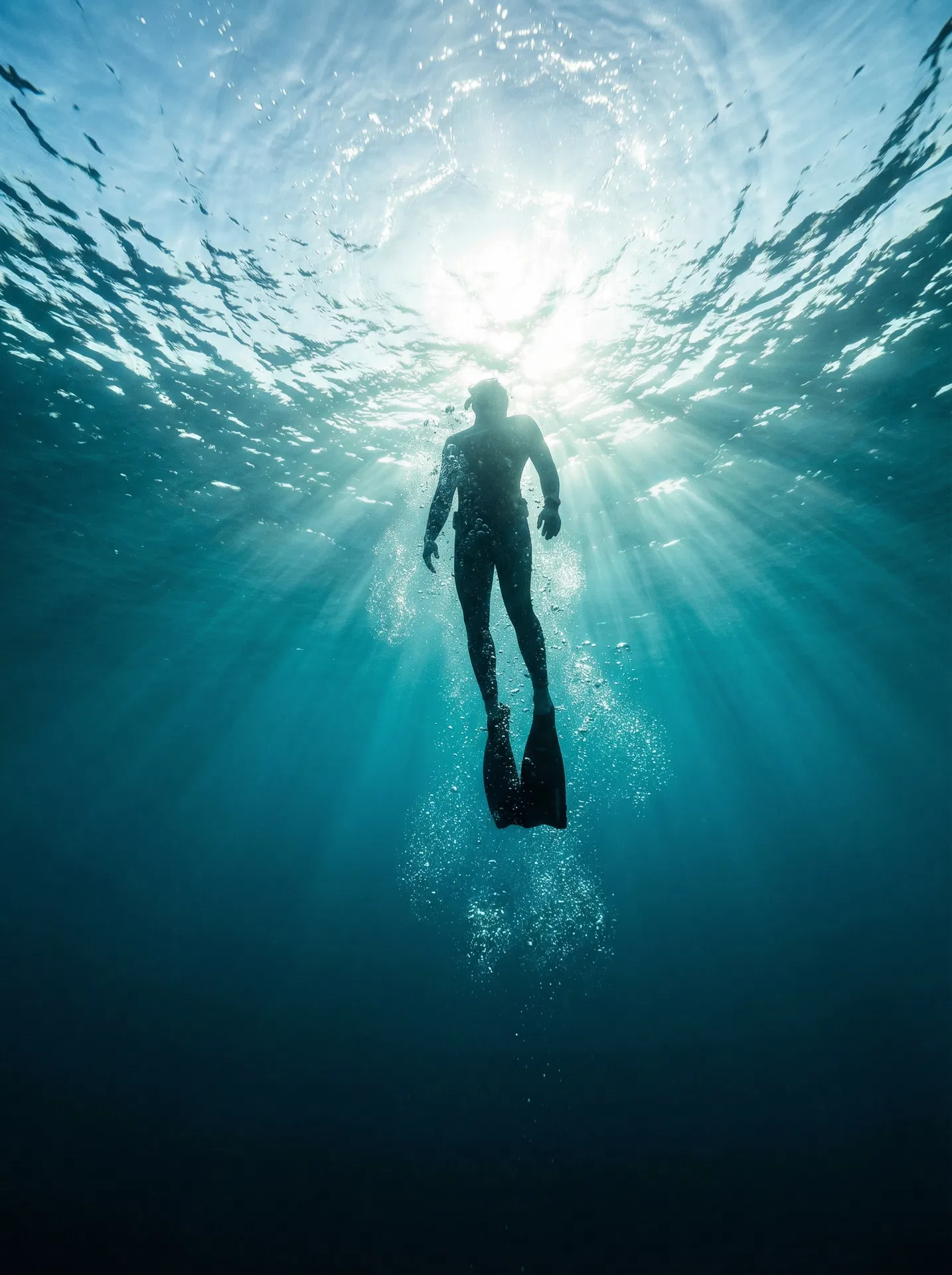 Freediver ascending through crystal-clear Mediterranean water with dramatic light rays