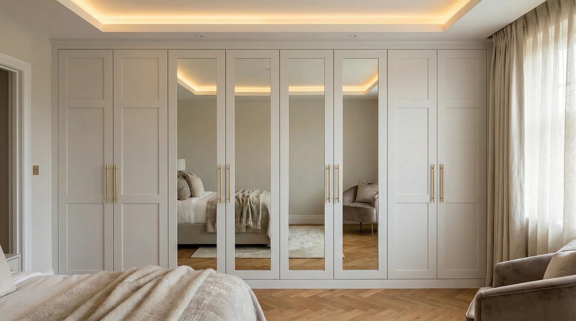 Bespoke floor-to-ceiling fitted wardrobes in a luxury Dorset bedroom — shaker-style doors in soft grey with gold bar handles and integrated mirrors