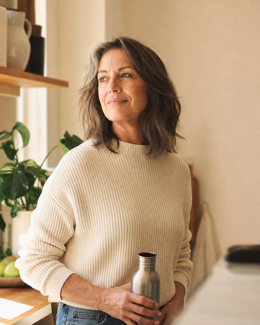 A confident woman in her 50s standing in a sunlit kitchen, calm and grounded.