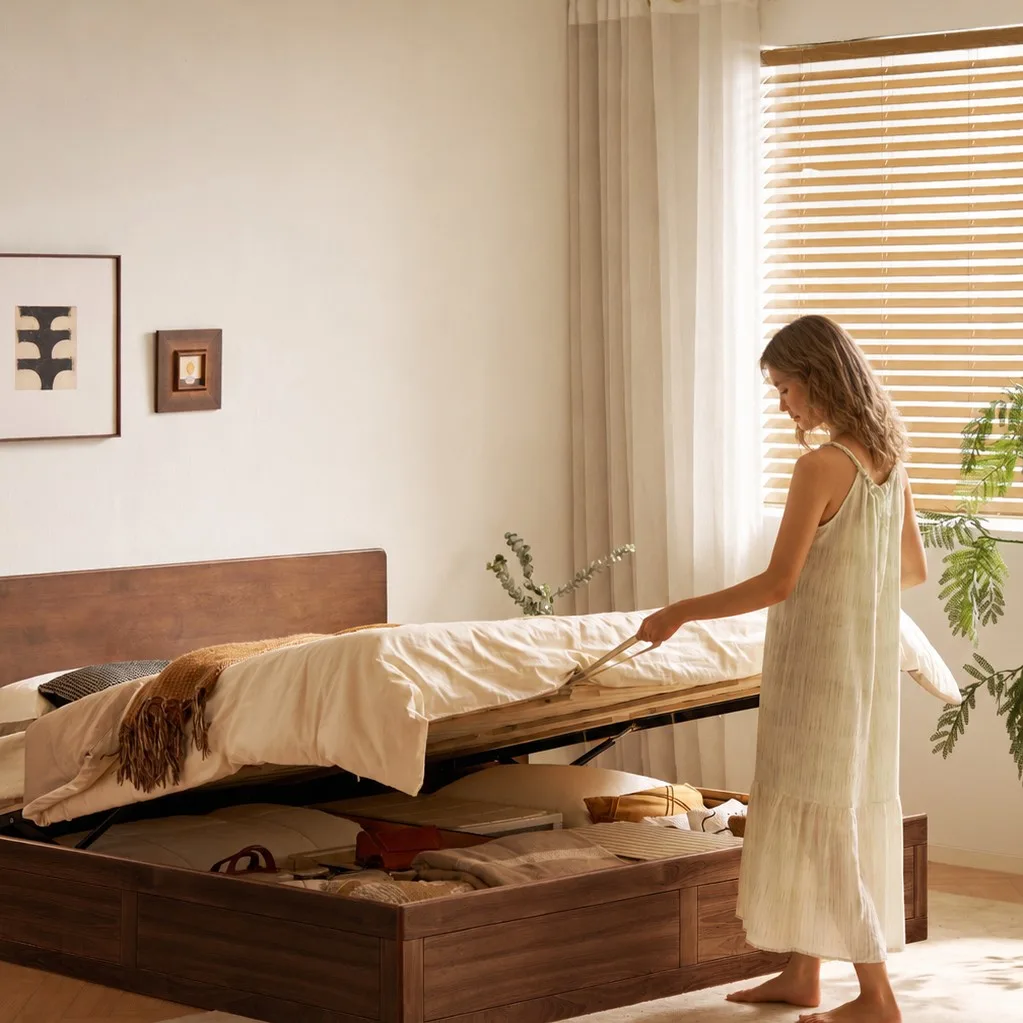 Woman lifting mattress on walnut rubberwood gaslift bed in bedroom, revealing underbed storage.