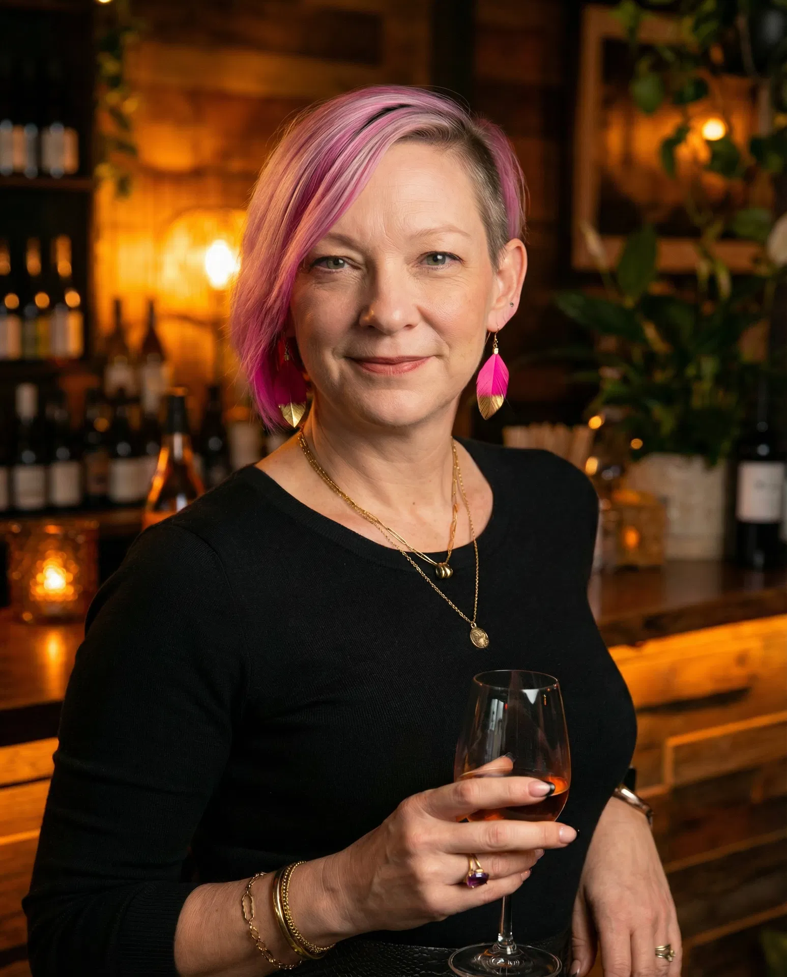 Hospitality owner persona with pink hair, gold-dipped feather earrings, black French-tip manicure, and layered gold jewelry representing Hospi's audience.
