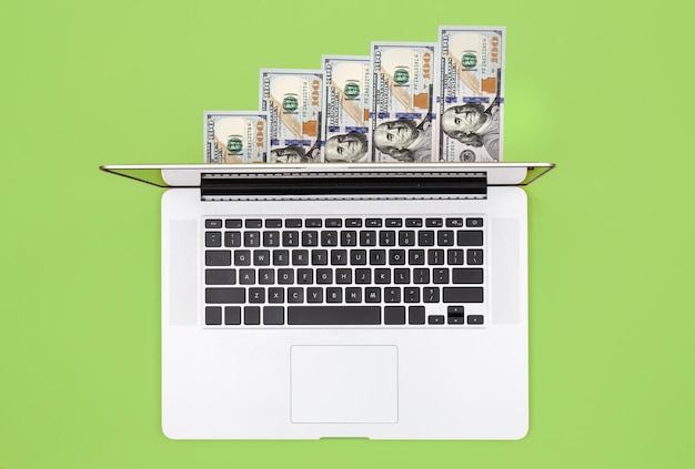 Laptop and dollar bills on color background flat lay
