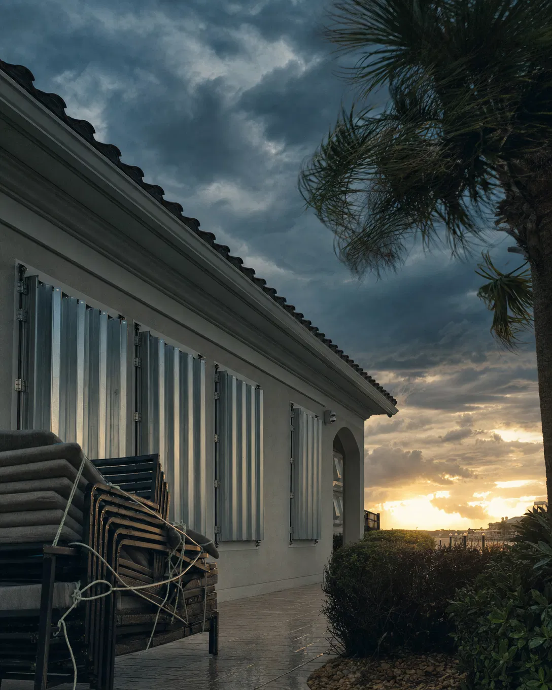 A Florida home with hurricane shutters partially closed under a stormy sky.