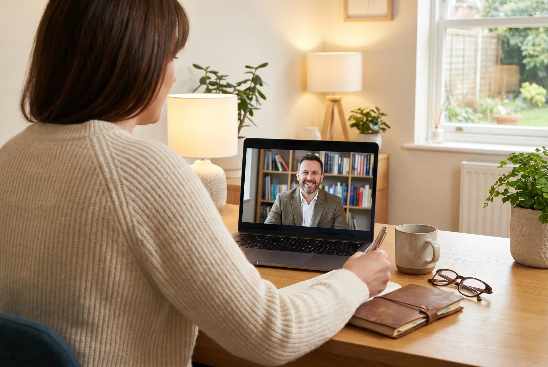 Professional on a video call with a career advisor, taking notes at a warm home office desk
