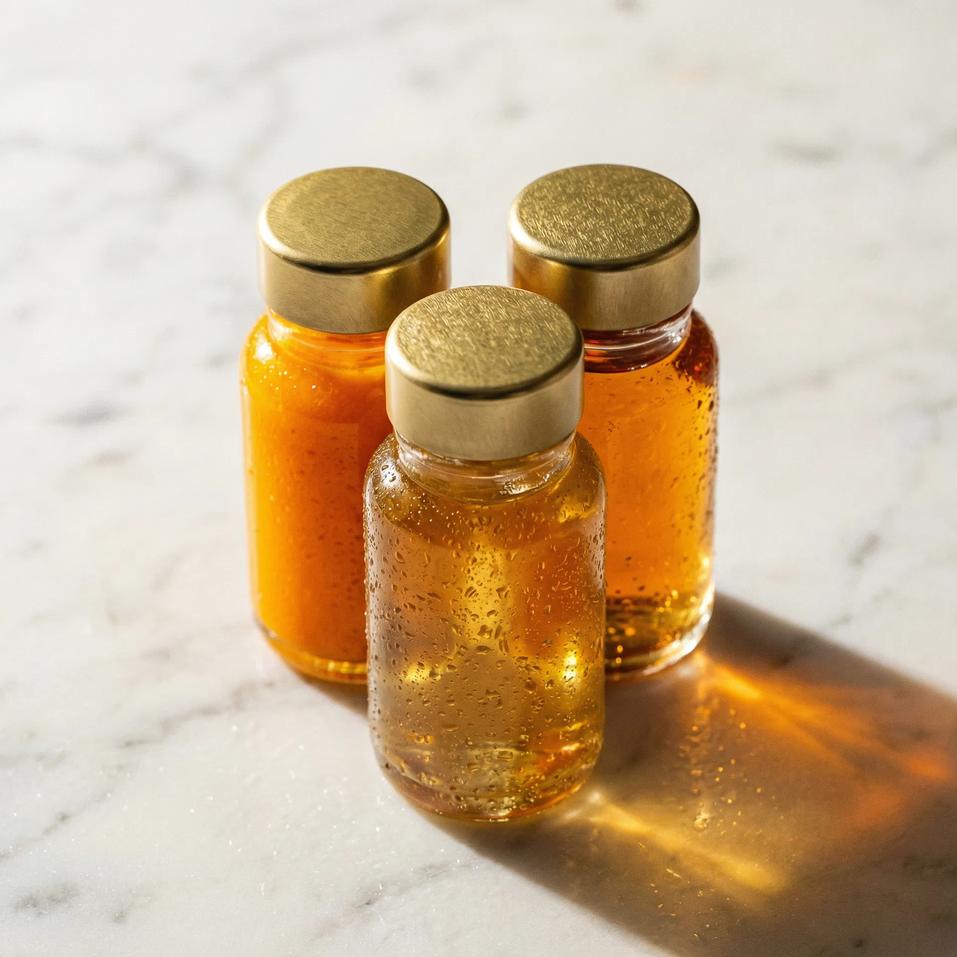 Three small wellness shot bottles with gold lids containing turmeric, ginger, and ACV shots on marble