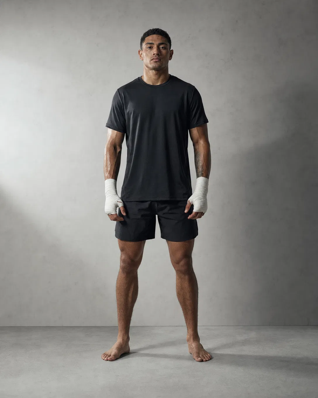 Combat-sports athlete in matte-black training kit with white hand-wraps — studio portrait