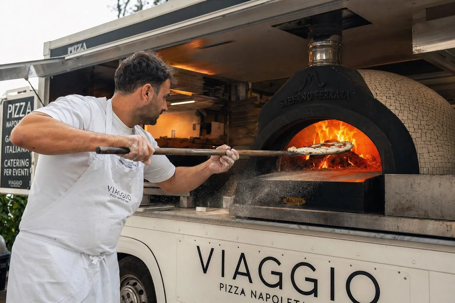 Chef launching pizza into wood-fired oven on food truck