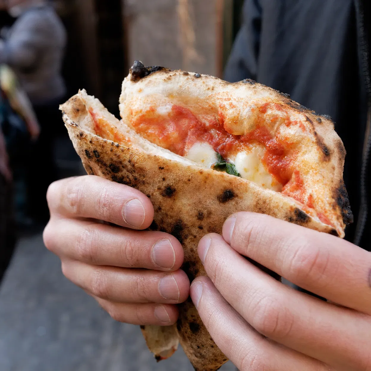 Hands holding a folded Neapolitan pizza slice