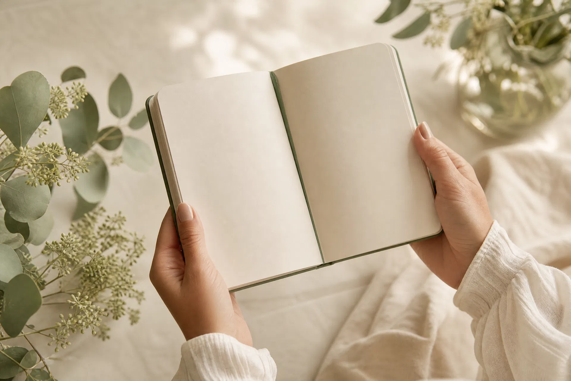 Woman's hands holding an open journal surrounded by eucalyptus and botanical greenery — PCOS PMOS hormonal health