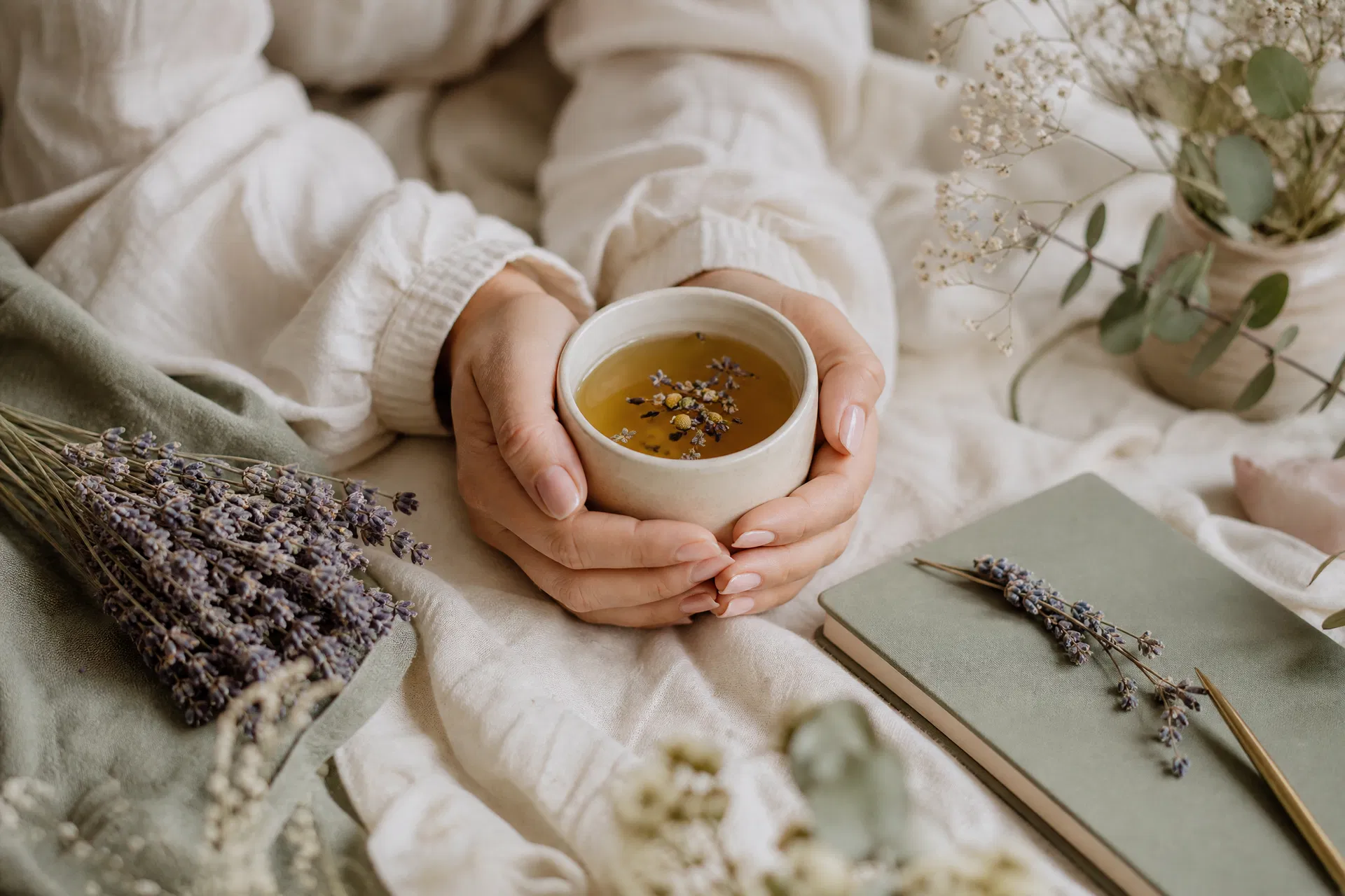 Hands cradling a warm mug of herbal tea surrounded by dried lavender and a journal — PMDD hormonal health nervous system