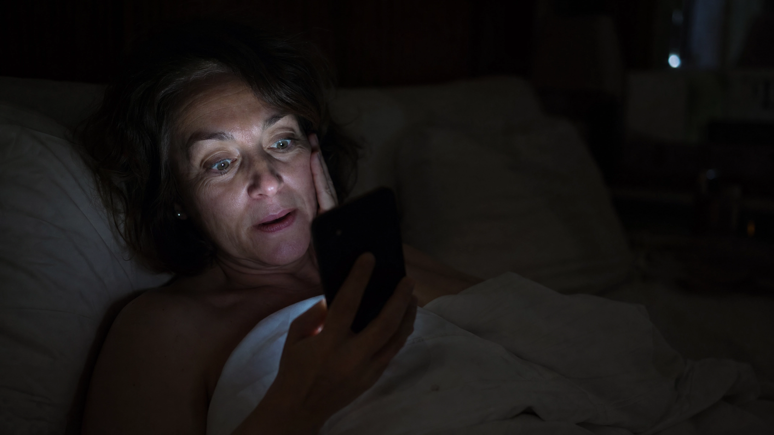 Mujer en cama a las 2am leyendo el móvil, descubrimiento en Facebook