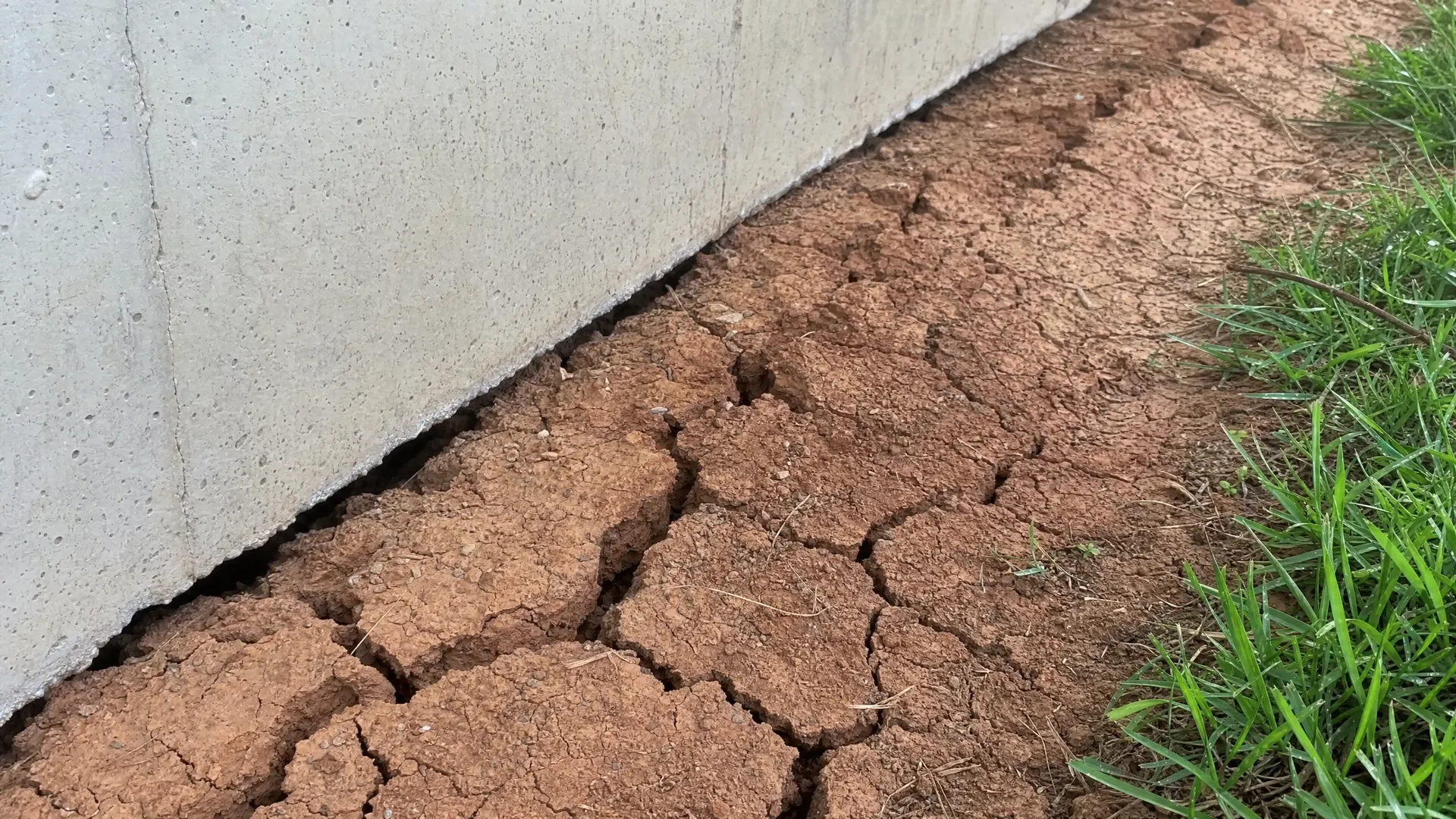 Cracked red clay soil next to a concrete home foundation in Rutherford County Tennessee