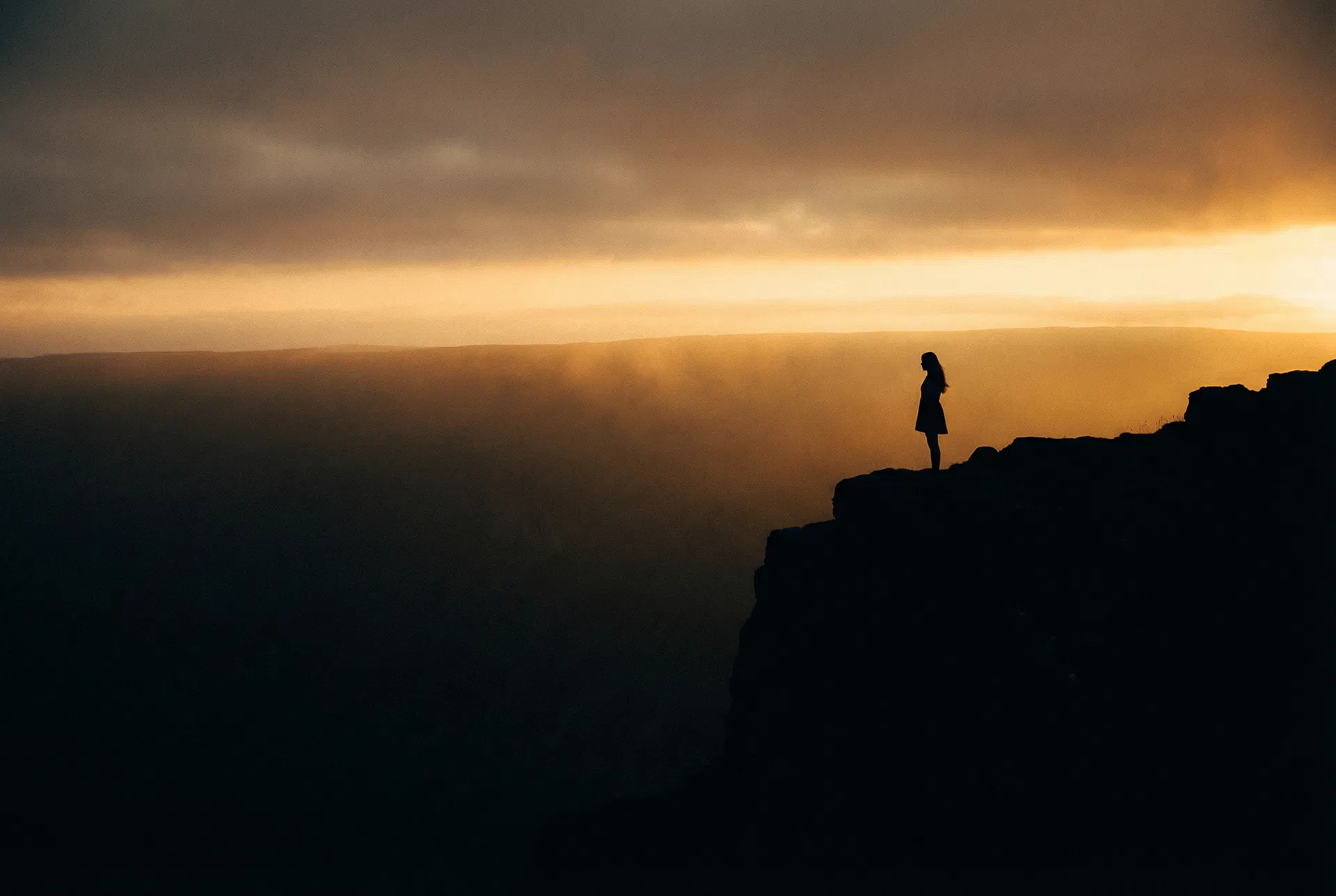 Woman standing at the edge of a cliff at dawn