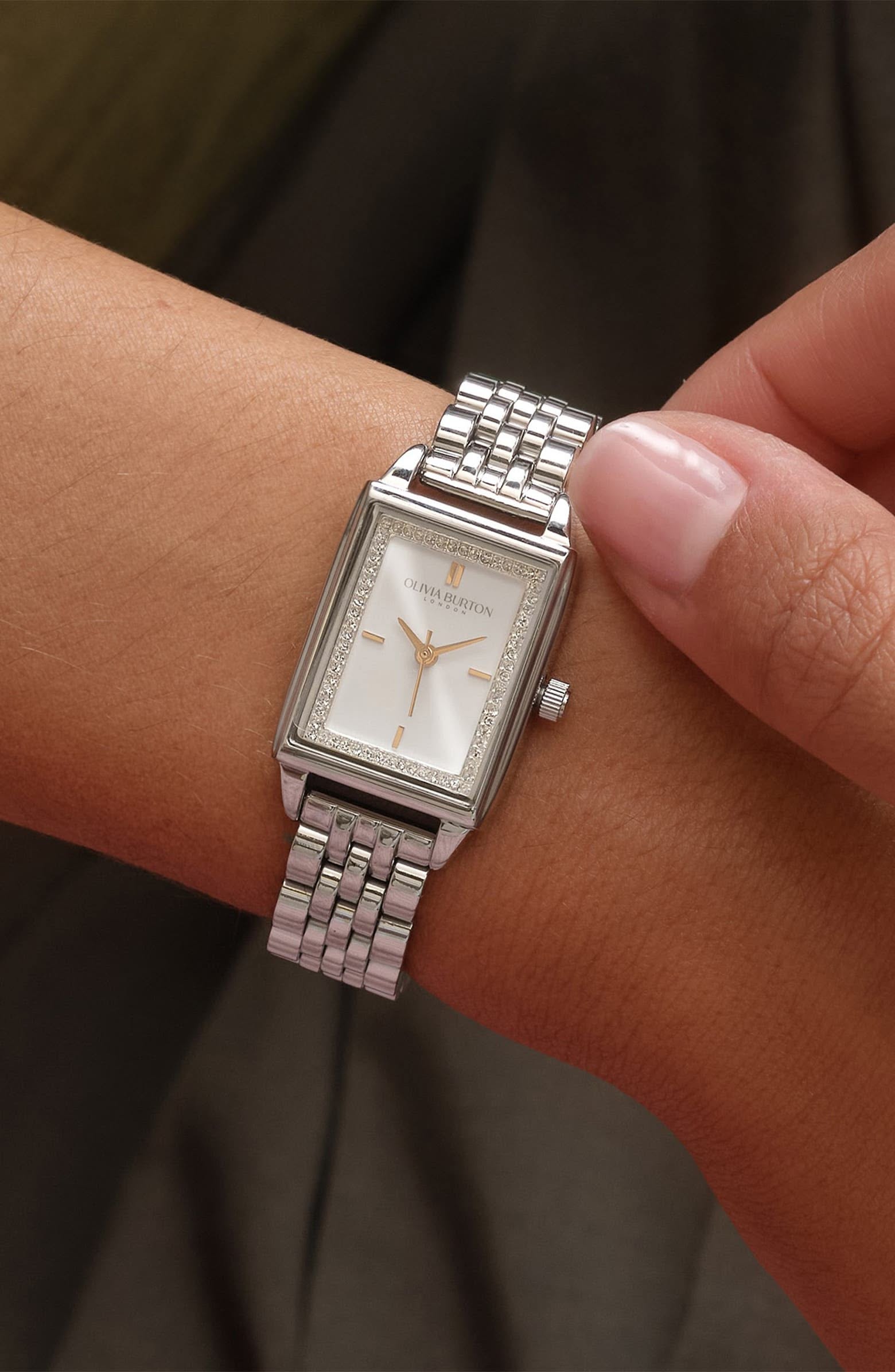 Olivia Burton silver wrist watch — rectangular case, crystal-set bezel, white dial, gold-tone hands and markers, link bracelet, crown
