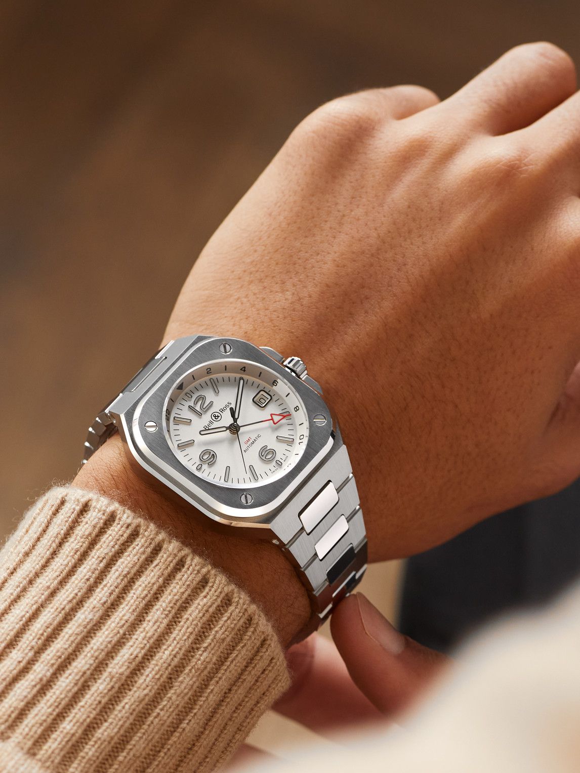 Bell & Ross silver and white wristwatch — integrated bracelet, square case with rounded corners, visible screws on bezel, white dial, GMT function, automatic movement