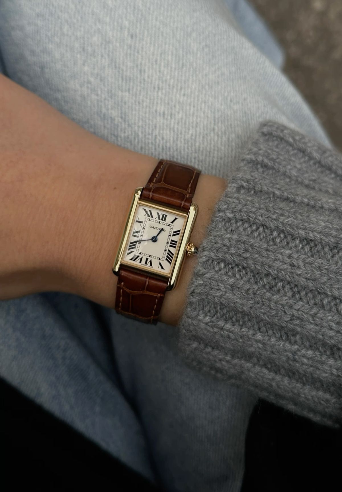 Cartier gold and brown watch — rectangular case, white dial, black Roman numerals, blue sword-shaped hands, fluted crown, alligator embossed leather strap