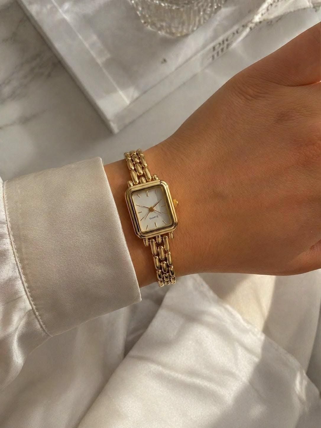 Classic gold-toned wrist watch — rectangular case, white dial, minimalist hour markers, three-link chain bracelet, 'QUARTZ' text on dial