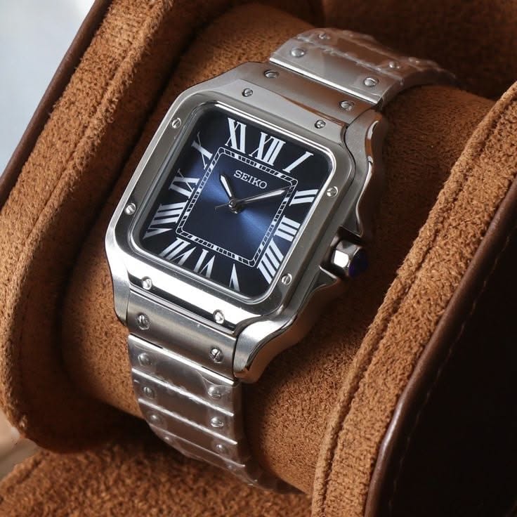 Seiko silver and blue wristwatch — square case, Roman numeral hour markers, blue sunburst dial, screw details on bezel and bracelet, fluted crown with blue cabochon