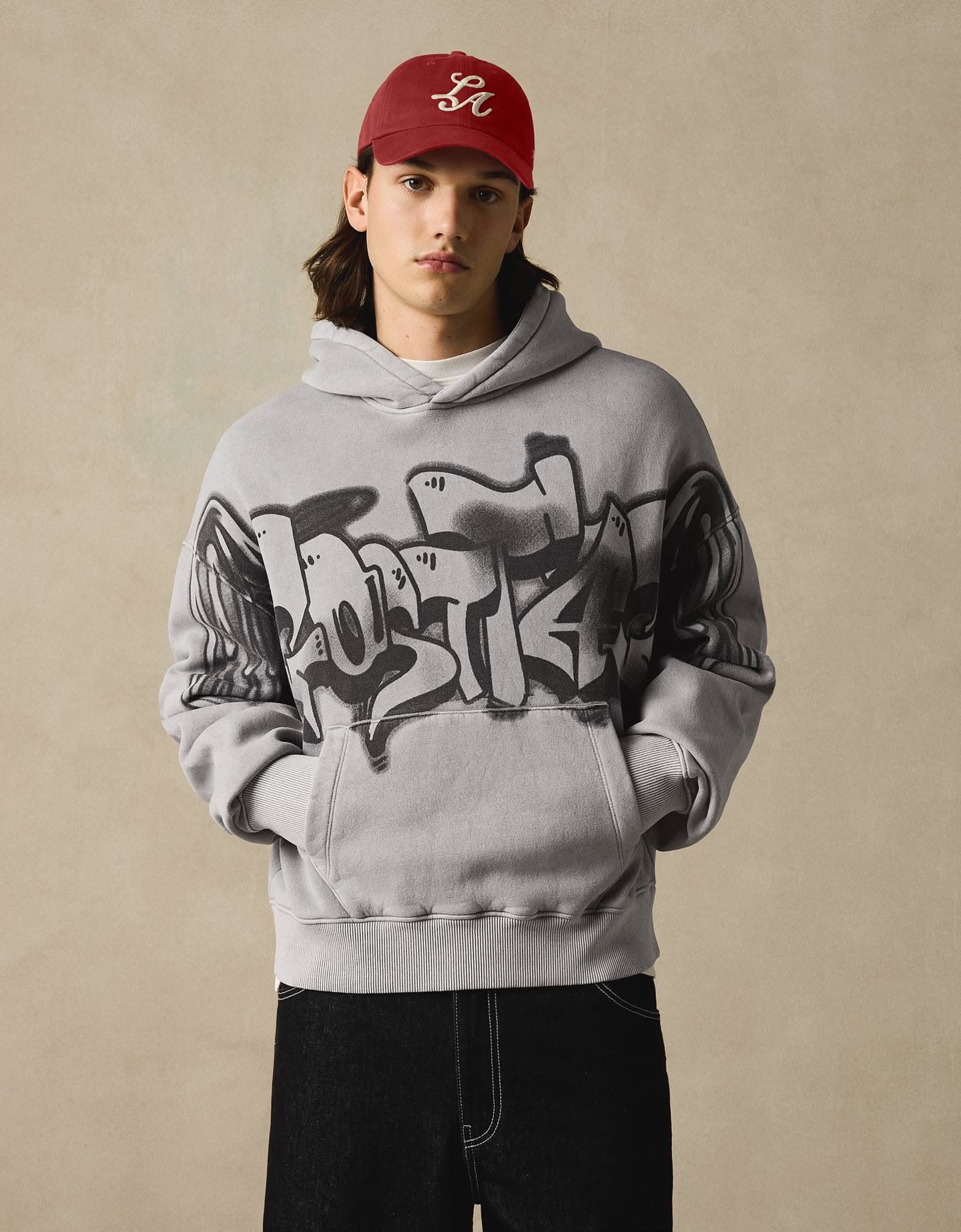 Streetwear light grey hoodie — drawstring hood, kangaroo pocket, ribbed cuffs and hem, distressed or faded wash effect, large black graffiti-style graphic print across the chest and sleeves