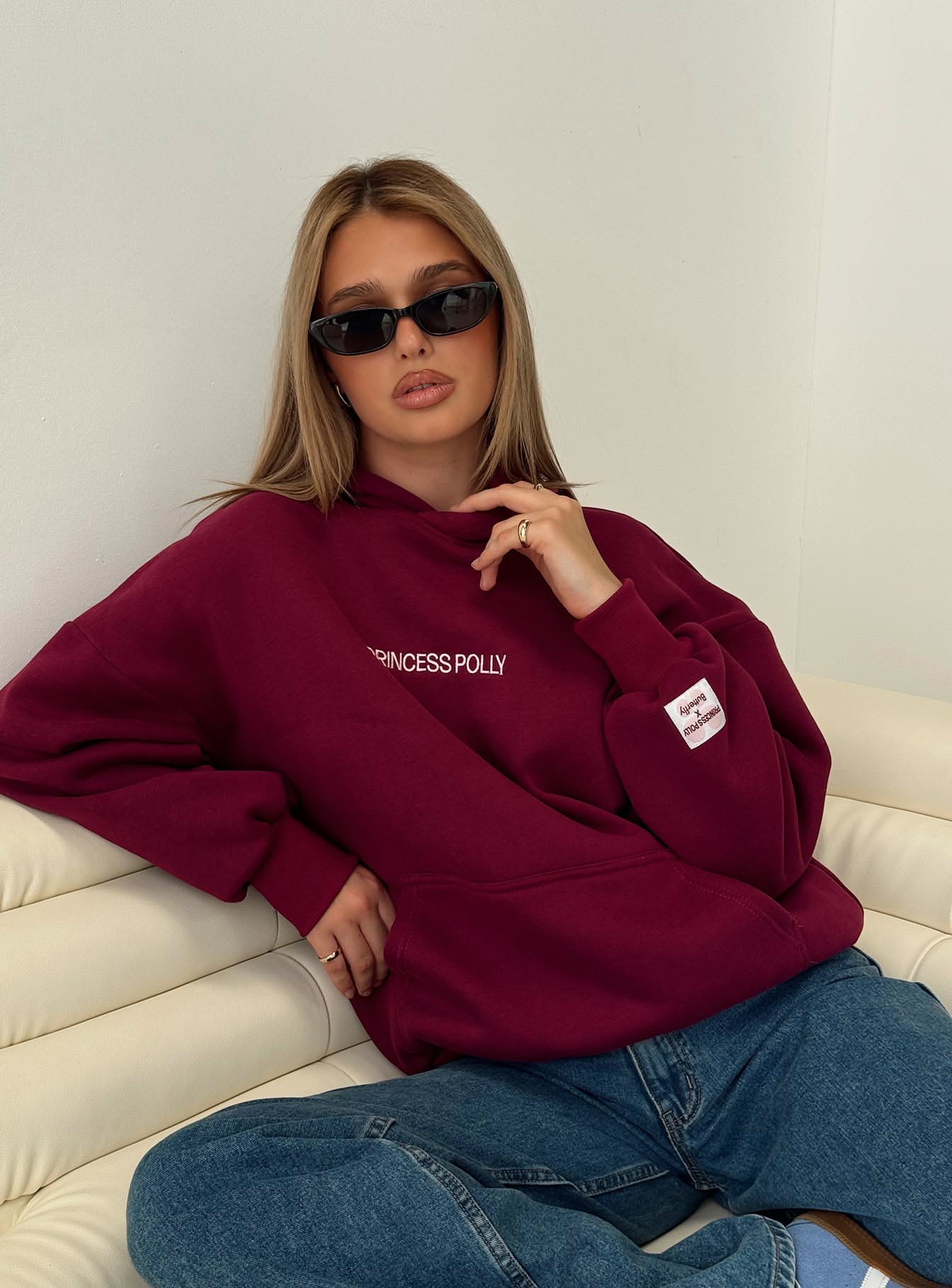 Princess Polly deep burgundy hoodie — drawstring hood, front kangaroo pocket, ribbed cuffs and hem, white 'PRINCESS POLLY' text print on the chest, small white and pink tag on the left sleeve cuff